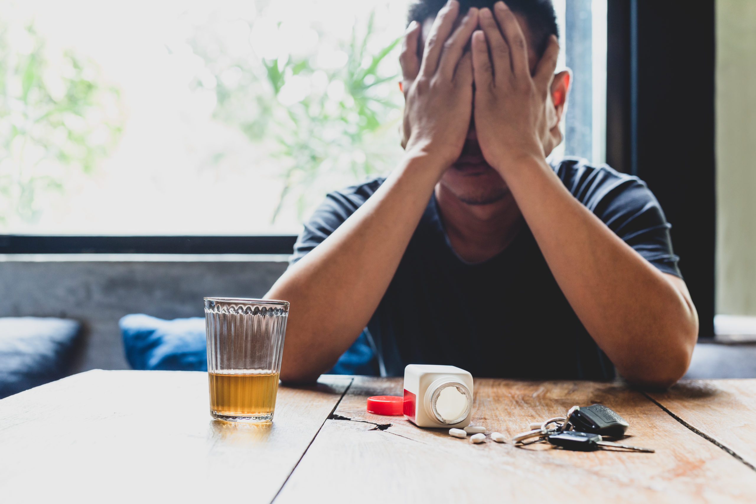 Depression man hand on his face with glass of alcohol and pills on the table.
